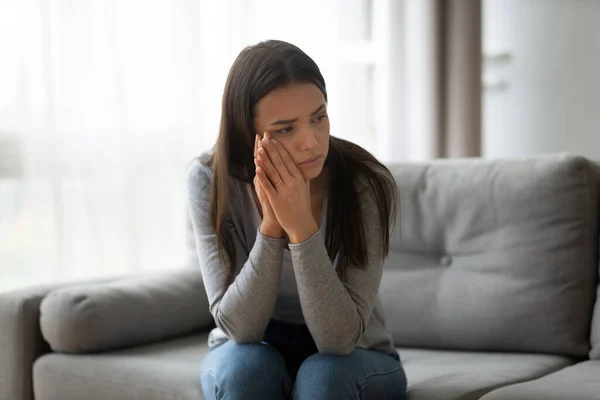 Thoughtful upset young woman sitting on couch at home — Stock Photo, Image