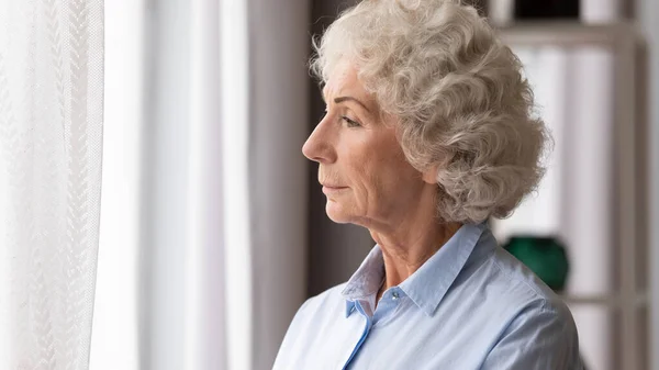 Old woman looking in window thinking lost in sad thoughts