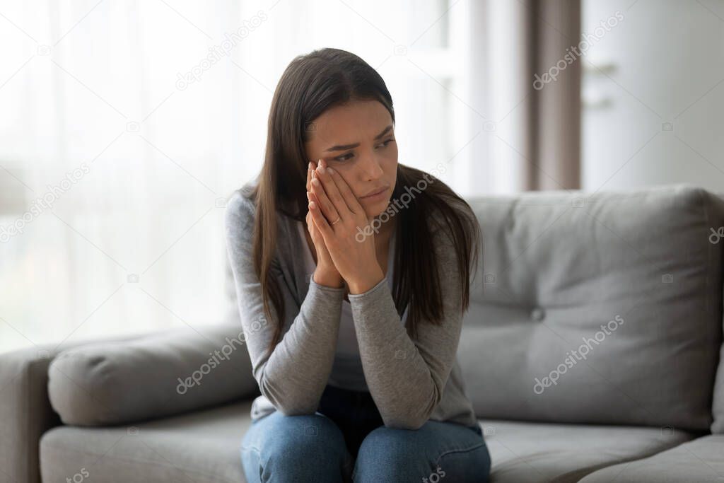 Thoughtful upset young woman sitting on couch at home