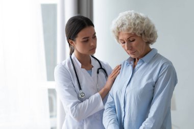 İlgili genç bakıcı evde yaşlı üzgün bir kadını rahatlatıyor.