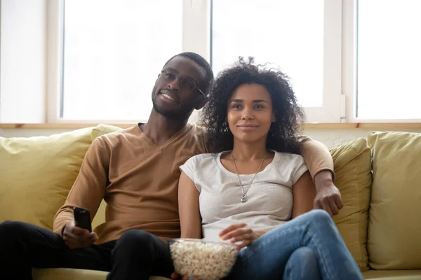 Pareja sentada en un sofá comiendo palomitas viendo películas en la televisión — Foto de Stock