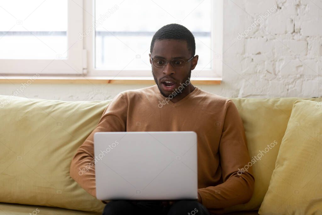 African ethnicity guy gawp at laptop screen feels shocked