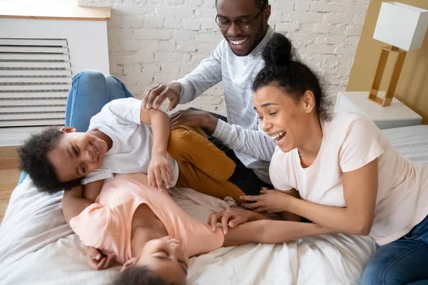 Casal africano jogando jogos ativos engraçados com crianças na cama — Fotografia de Stock