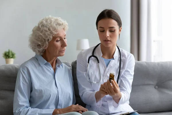 Nurse seated on couch explain to old patient pills dosage