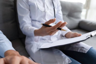 Yakın plan kadın terapist elinde dosya tutarak yaşlı bir hastayla konuşuyor.