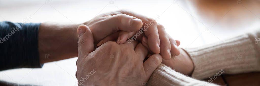 Middle-aged couple sit indoors holding hands closeup horizontal photo
