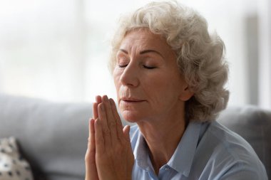 Yaşlı bir kadın dua ediyor. Gözleri kapalı, avuç içlerini kavuşturmuş.
