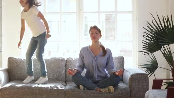 Während Tochter Spaß beim Springen auf Sofa hat, macht Mutter Yoga — Stockvideo