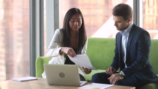 Asian european business partners sitting on couch discussing contract details — Stock Video