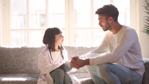 Αξιολάτρευτη κόρη με λευκό παλτό που παίζει τον γιατρό με τον πατέρα — Αρχείο Βίντεο