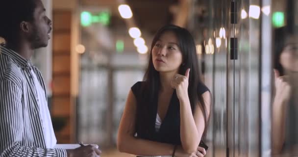 Серьёзная азиатка-лидер инструктирует чернокожего стажера, стоящего на посту — стоковое видео