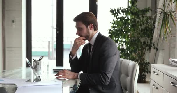 Ernsthaft besorgter Geschäftsmann im Anzug forscht am Laptop — Stockvideo