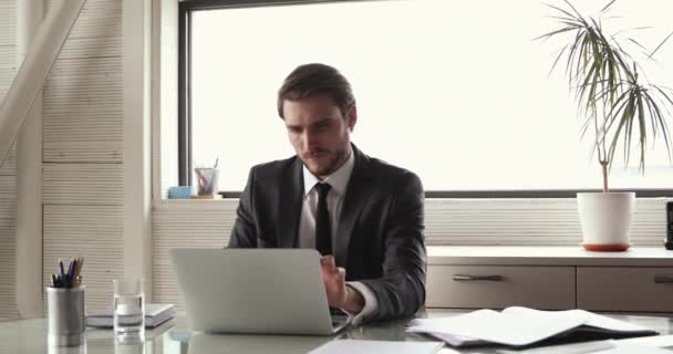 Serious concentrated young businessman working on laptop at workplace — Stock Video