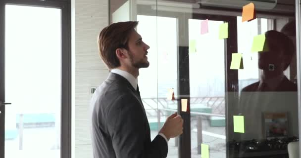 Executive op zoek naar plakkerige notities op glas muur planning strategie — Stockvideo