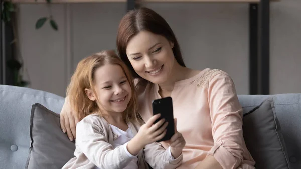 Feliz jovem mãe e pequena filha usar smartphone juntos — Fotografia de Stock