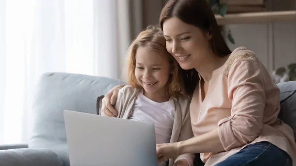 Smiling mom and little daughter using laptop at home