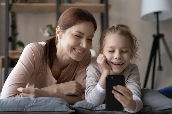 Улыбающиеся мама и маленькая дочь смотрят видео на камеру вместе — стоковое фото