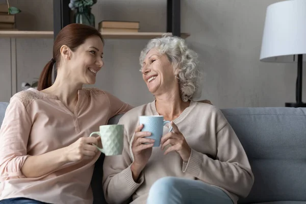 Счастливая старшая мама и взрослая дочь пьют чай дома — стоковое фото
