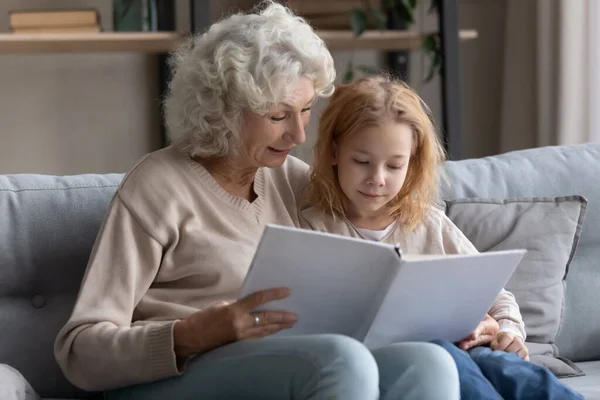 Zorgzame senior grootmoeder lezen boek met kleine kleindochter — Stockfoto