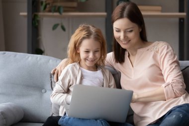 Gülümseyen genç anne ve küçük kız dizüstü bilgisayar kullanıyor.