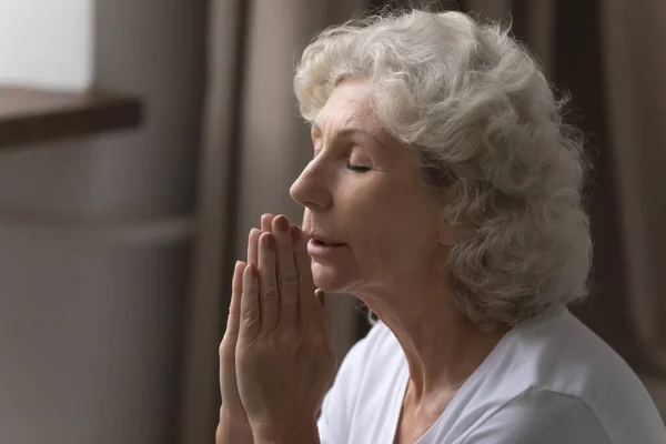 Religious elderly woman praying to god at home — Stock Photo, Image