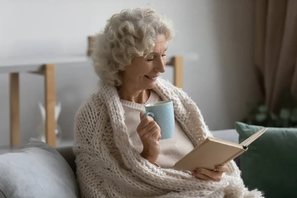 Mutlu kıdemli kadın evde kitap okuyarak rahatlıyor. — Stok fotoğraf