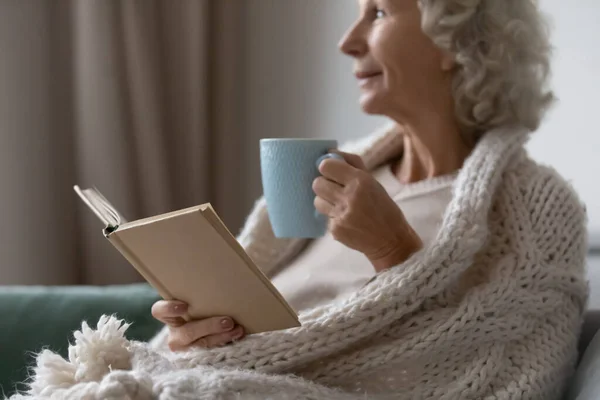 Mujer mayor soñadora relajándose con libro en la sala de estar — Foto de Stock