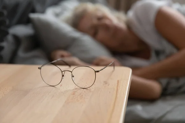 Primer plano de las gafas femeninas maduras en la mesita de noche —  Fotos de Stock