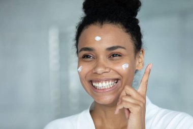 Yüzünde nemlendirici yüz kremi olan, gülümseyen Afrikalı Amerikalı kadın.
