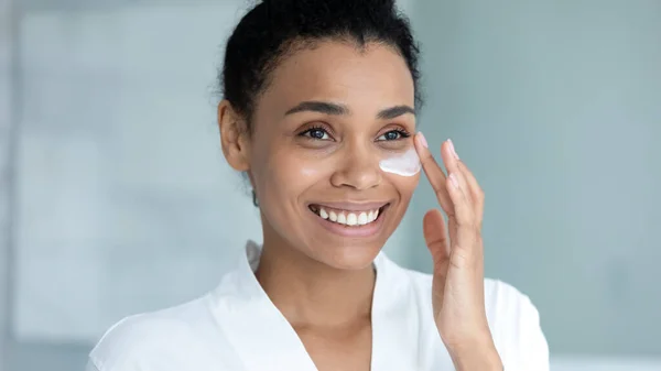 Close up sorridente donna afroamericana applicando crema idratante — Foto Stock
