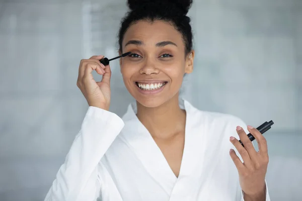 Foto de la cabeza retrato sonriendo mujer afroamericana aplicando rímel negro —  Fotos de Stock