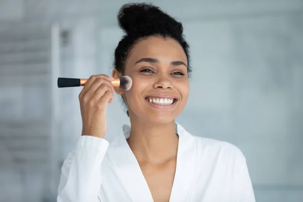 Tiro na cabeça sorrindo mulher afro-americana usando escova de cosméticos — Fotografia de Stock