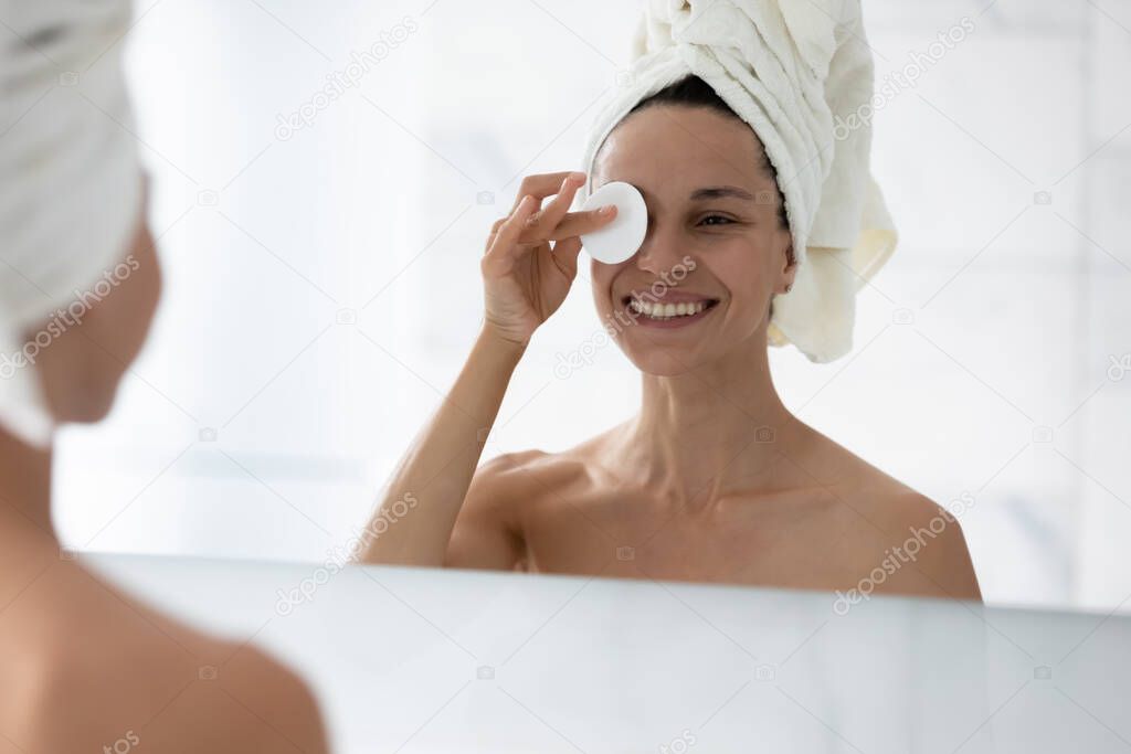 Head shot smiling woman removing face makeup, using cotton pad