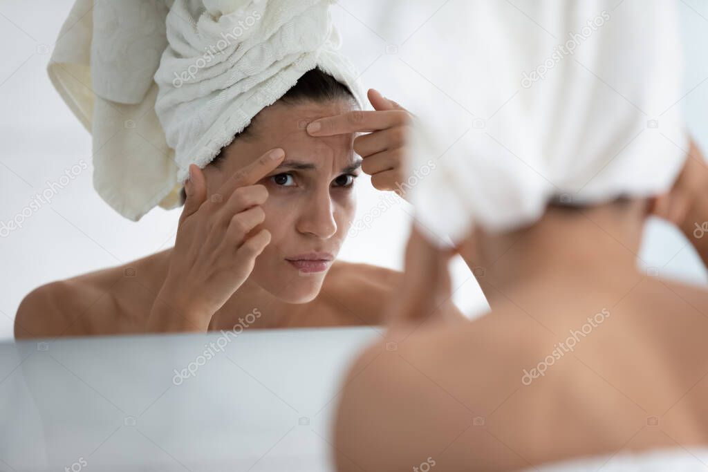 Close up unhappy woman squeeze pimple on forehead