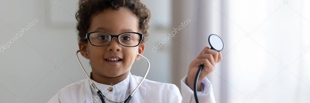 African boy wearing white coat uniform holding stethoscope playing doctor