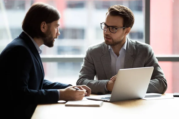 Twee zelfverzekerde zakenlieden zitten aan het bureau te praten over het oplossen van gemeenschappelijke problemen — Stockfoto