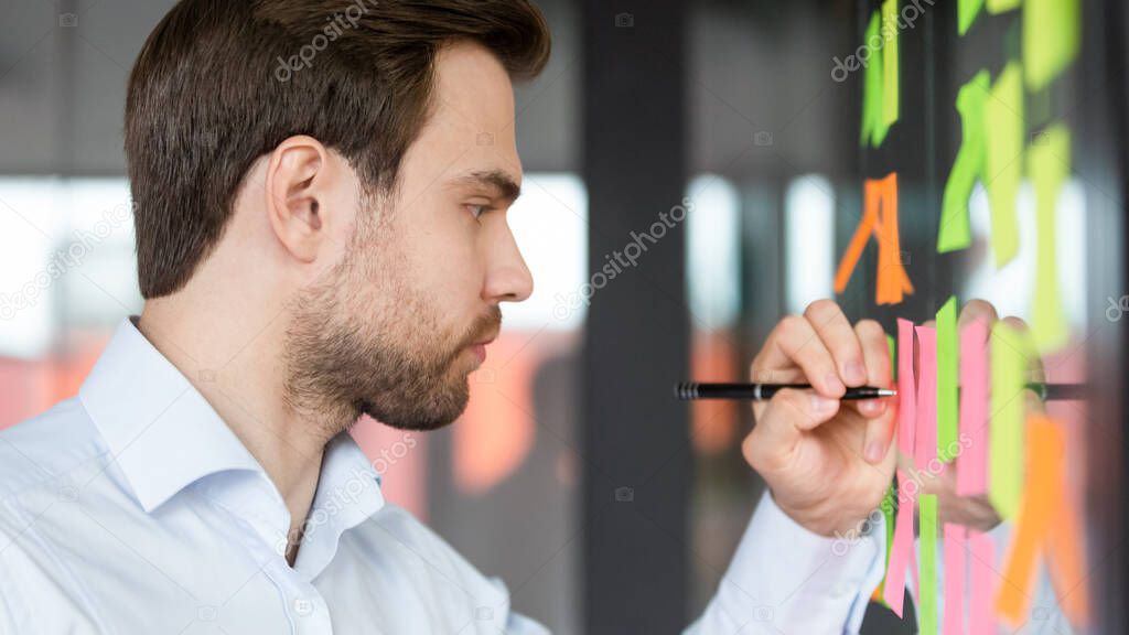 Focused businessman writing on sticky notes attached on glass wall