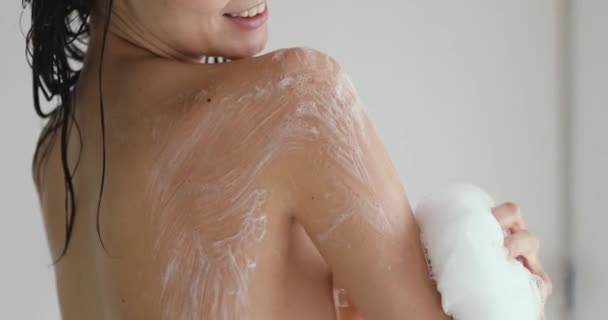 Молодая 20-летняя женщина использует мочалку для ванны в душе . — стоковое видео