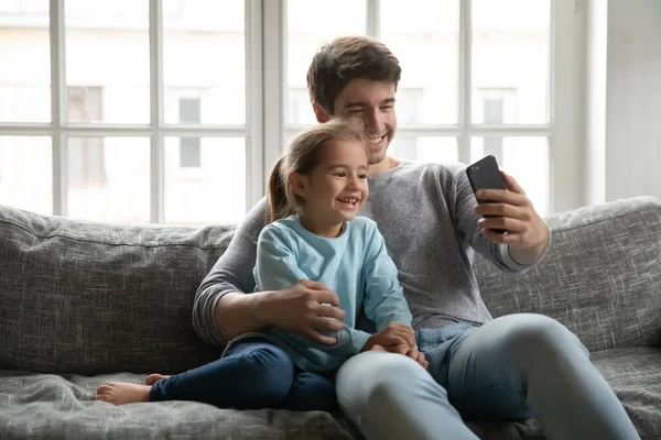 Sonriente papá joven y su hija pequeña hacen selfie en el teléfono inteligente —  Fotos de Stock