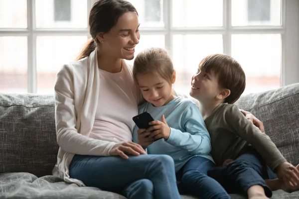 Genç anne kanepede rahatla. Çocuklarla cep telefonu kullan. — Stok fotoğraf