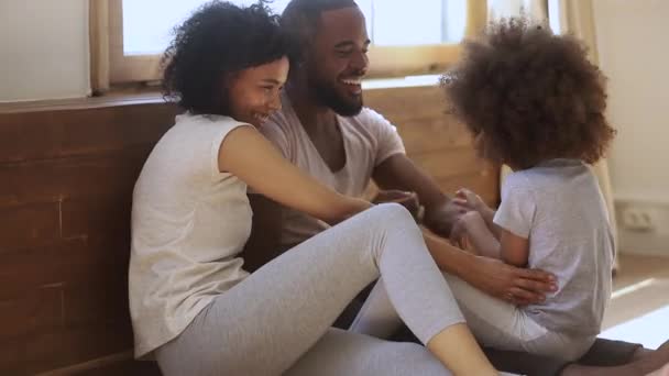 Happy black parents and child daughter tickling sit on floor — Stockvideo