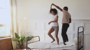 Happy young romantic african couple holding hands dancing on bed