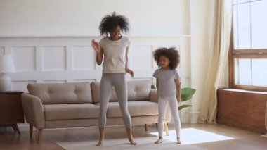 Active african mom and kid daughter jumping dancing at home