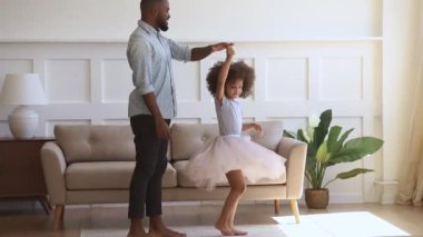 Happy african dad dancing with his child daughter princess