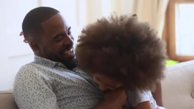 Happy african father and child daughter tickling sit on sofa