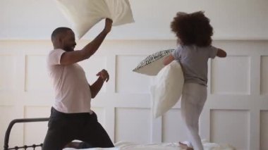 Cute daughter playing pillow fight on bed with black father