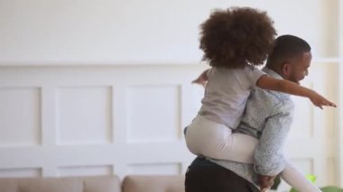 Happy black dad giving kid daughter piggyback ride at home