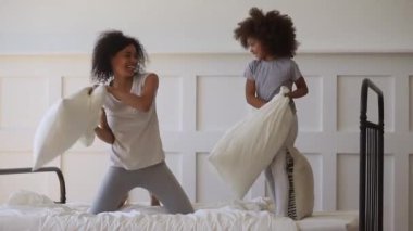 Happy african mom and daughter playing pillow fight on bed