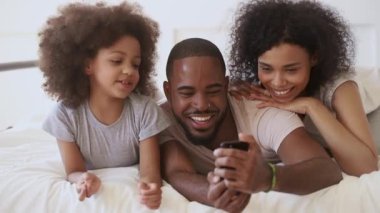 African parents with daughter using funny mobile app in bed