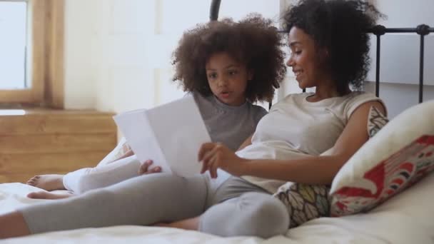 Hija africana contando cuento de hadas a madre sosteniendo libro en la cama — Vídeo de stock